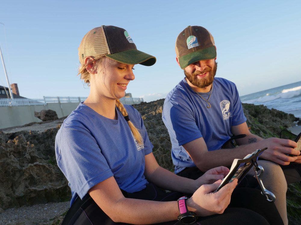 two people sitting on beach looking at book